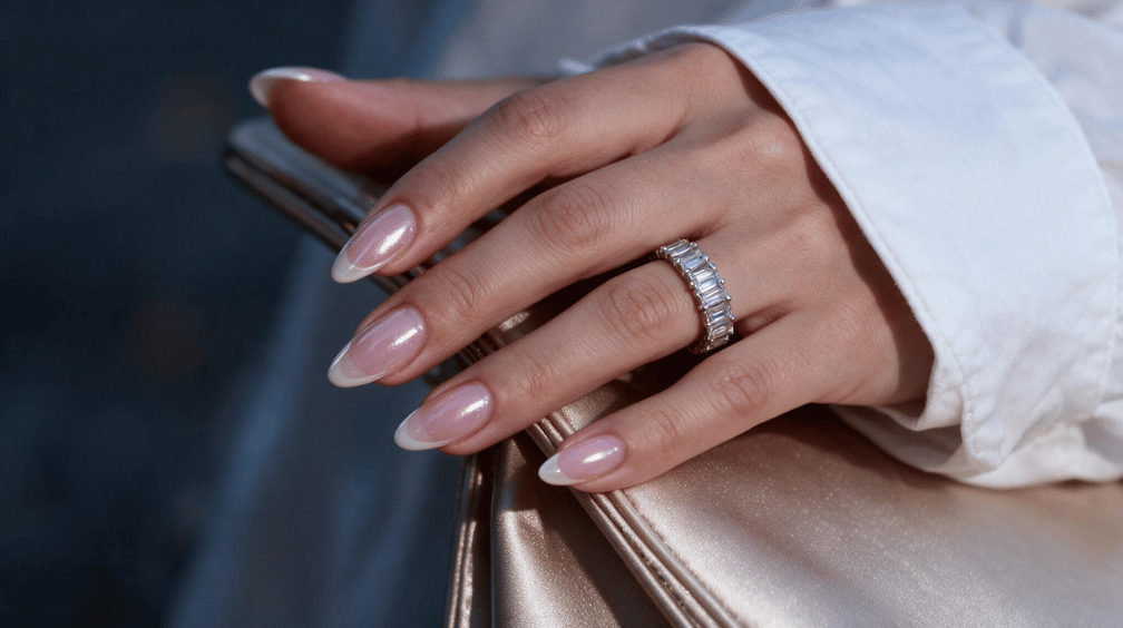 glossy pink chrome almond nails with pale french tips resting on a champagne clutch
